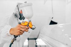 a man in white coat holding a paint roller and spraying yellow paint on the side of a car