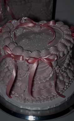 a white cake with pink ribbon and heart decorations on the top is sitting on a silver platter