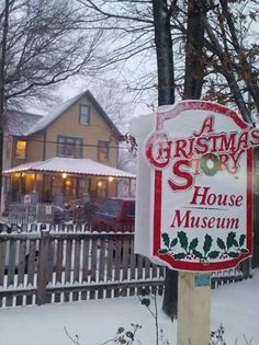 a christmas story house museum sign in front of a wooden fence and tree with snow on it