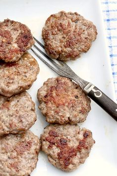 several hamburger patties on a white plate with a knife and fork next to them