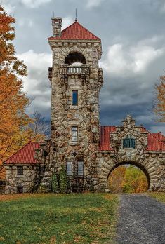 an old stone building with a red roof surrounded by trees and leaves in the fall