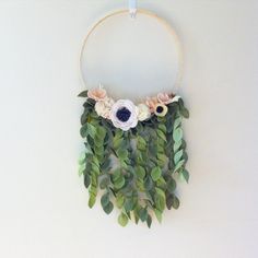 a white flower and green leaves hanging from a hoop on the side of a wall