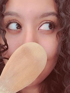 a close up of a person with a spoon in front of her face and a wooden spatula over their mouth