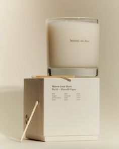 a white candle sitting on top of a box next to a wooden stick in front of it