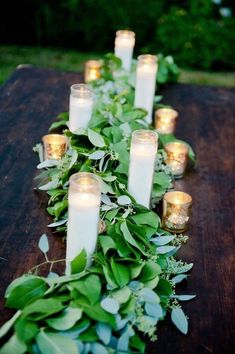 candles are lined up on a table with green leaves and greenery around the edges