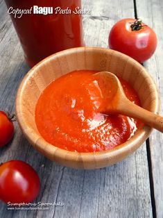 a wooden bowl filled with tomato sauce next to tomatoes