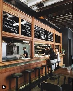 two people are standing at the bar in front of the chalkboard menus on the wall