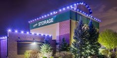 the storage building is lit up at night with lights on it's sides and trees in front