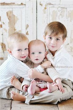 three young children are sitting on the floor and posing for a photo with their arms around each other