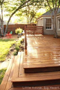 a wooden deck with steps leading up to the house and trees in the back yard