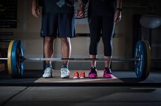 two people standing next to each other with their feet on a barbell in front of them