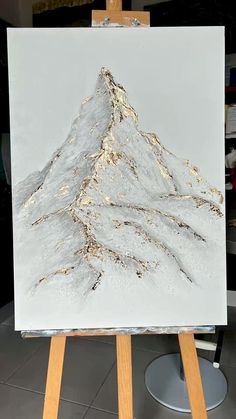 an easel with a painting on it that has a mountain in the middle and gold paint