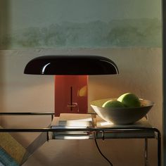 two green apples in a white bowl on a table next to a black light fixture