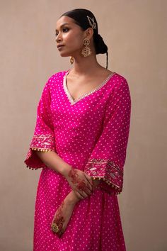 Hot pink silk A-line kurta with all over bandhani pattern, side lacing tie-ups, zardozi embroidered bell sleeves border and leaf neck. Paired with straight fit pant with embroidered border. Components: 2 Pattern: Embroidered Type Of Work: Bandhani Pattern and Zardozi Work Neckline: Leaf Neck Sleeve Type: Bell Sleeves Fabric: Silk Color: Pink Other Details:  Drop tassel details Kurta Closure: Side lacing tie-ups Occasion: Sangeet,Mehendi and Haldi - Aza Fashions Bandhani Suit Design, Kurta Sets For Women Party Wear, Bell Sleeves Suit, Bandhej Kurti Designs, Bandhani Blouse Pattern, Bandhani Suits Design, Bandhani Dress Design, Bandhani Anarkali Dress