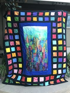 a large colorful quilt hanging on the side of a building with buildings painted on it