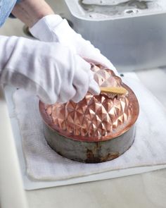 a person in white gloves is cleaning a copper pot