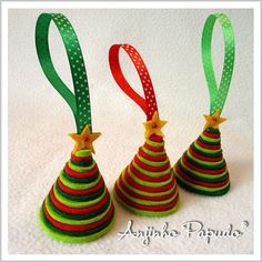 three small christmas trees with green, red and yellow ribbons on them are lined up against a white background