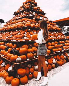 a woman standing in front of a pile of pumpkins