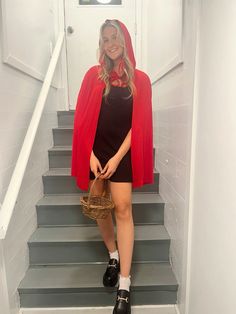 a woman in black dress and red cape standing on stairs holding a wicker basket