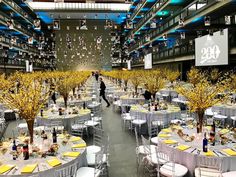 a large room filled with tables covered in white tablecloths and yellow tree decorations