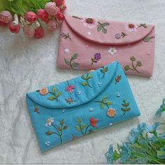 two purses sitting on top of a white table next to pink and blue flowers