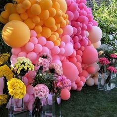 a bunch of balloons that are on the side of a wall with flowers in vases