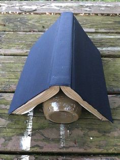 an open book sitting on top of a wooden table next to a glass vase with water in it