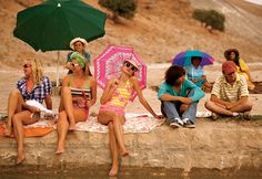 four women sitting on the ground with umbrellas over their heads and one woman holding an umbrella