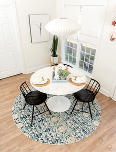 a white table with two black chairs and a potted plant in the middle on top of it