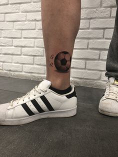 a person with a soccer ball tattoo on their leg and foot, standing next to a brick wall