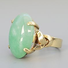 "Vintage 1970's Cabochon Jade Ring. This piece is a Hallmarked 14K yellow gold cast fashion lady's ring size 5 with a bright polish finish weighting 6.51 grams. The featured lady's ring has a straight shank with split knot ribbon shoulders, small gallery and one prong set oval Cabochon cut natural Jade measuring 17.88 mm x 12.75 mm approx 10.76 ct with bright hue middle green color. This piece is a real beauty with a height from the bridge of 7.42 mm. Also Hallmarked LC. This piece is in very go Gold Solitaire Ring, Jade Ring, Natural Jade, 14k Gold Ring, Green Stone, Oval Cabochon, Cleaning Jewelry, Solitaire Ring, Gold Ring