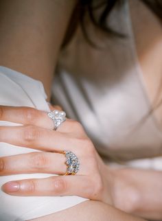 a woman's hand with two diamond rings on her left and the other hand holding an engagement ring