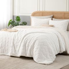 a bed with white comforter and pillows in a room next to a potted plant