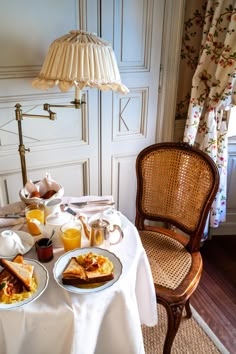 two plates of breakfast food on a table with a chair and lamp in the background