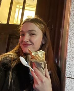 a young woman eating a piece of pizza and holding a spoon in her right hand