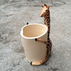 a ceramic giraffe sitting inside of a cup on the ground with it's legs sticking out