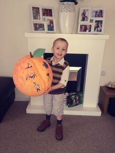 a young boy holding a pumpkin in front of a fireplace