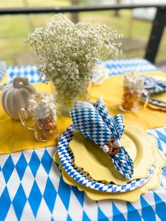 a blue and white table cloth with yellow plates, napkins and flowers on it