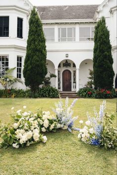 two white flowers are in front of a large house with trees and bushes around it