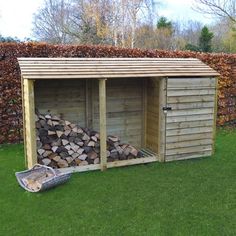 a wooden shed with logs stacked in the front and side by side on grass area