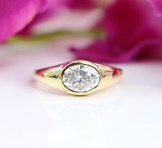 a yellow gold ring with a round diamond on it and pink flowers in the background