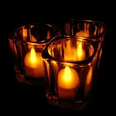 four lit candles in glass containers on a black background