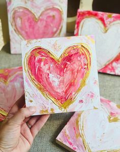 a hand holding up a piece of art that has been painted with pink and gold paint