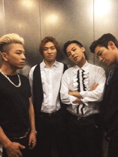 four young men standing next to each other in front of a metal wall with their arms crossed