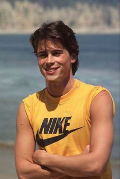 a young man standing on top of a beach next to the ocean wearing a yellow shirt