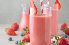 three glasses filled with pink smoothie next to strawberries and blueberries on the table