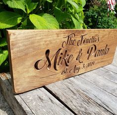 a wooden sign sitting on top of a wooden table next to green plants and flowers