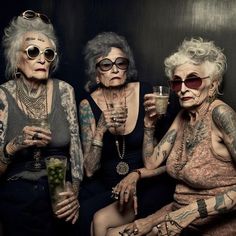 three older women sitting next to each other with tattoos on their arms and legs, one holding a drink in her hand