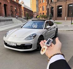 a person holding a cell phone in front of a silver sports car on the street