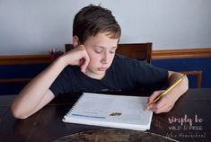 a young boy sitting at a table with a notebook and pen in front of him